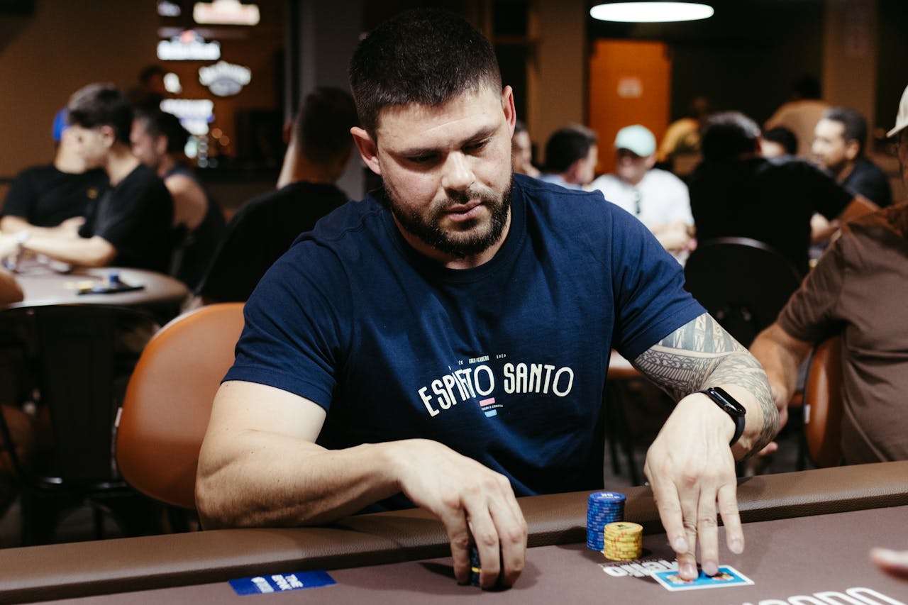 About An adult man plays poker at a casino table, focusing on his hand and poker chips.